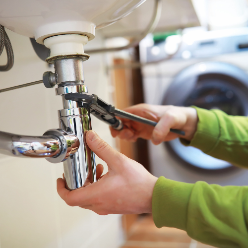 A pipe underneath a sink being tightened by a wrench