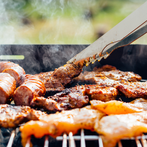 Meats on a grill being rotated by metal tongs